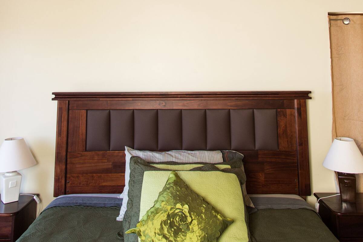 A wooden ceiling with a light fixture, a bed with a wooden headboard, and two bedside tables with lamps.