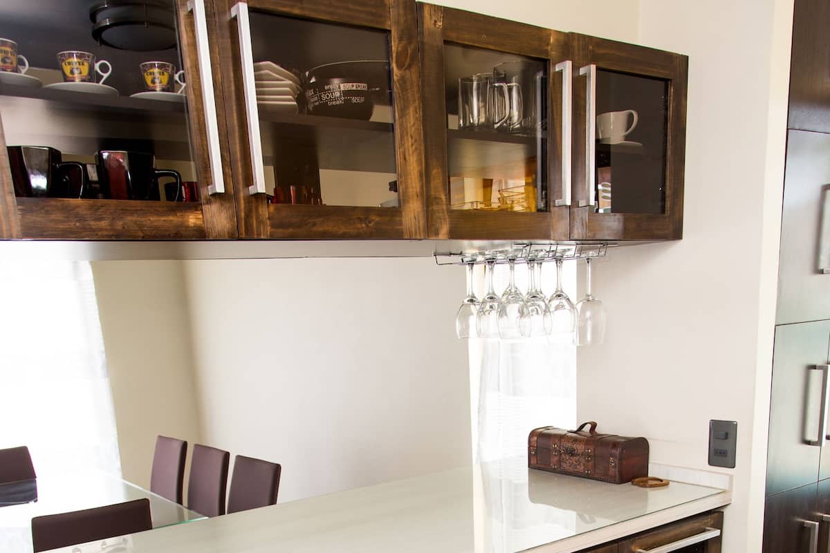 A kitchen with a white countertop, wooden cabinets, and a glass door with a wine rack.