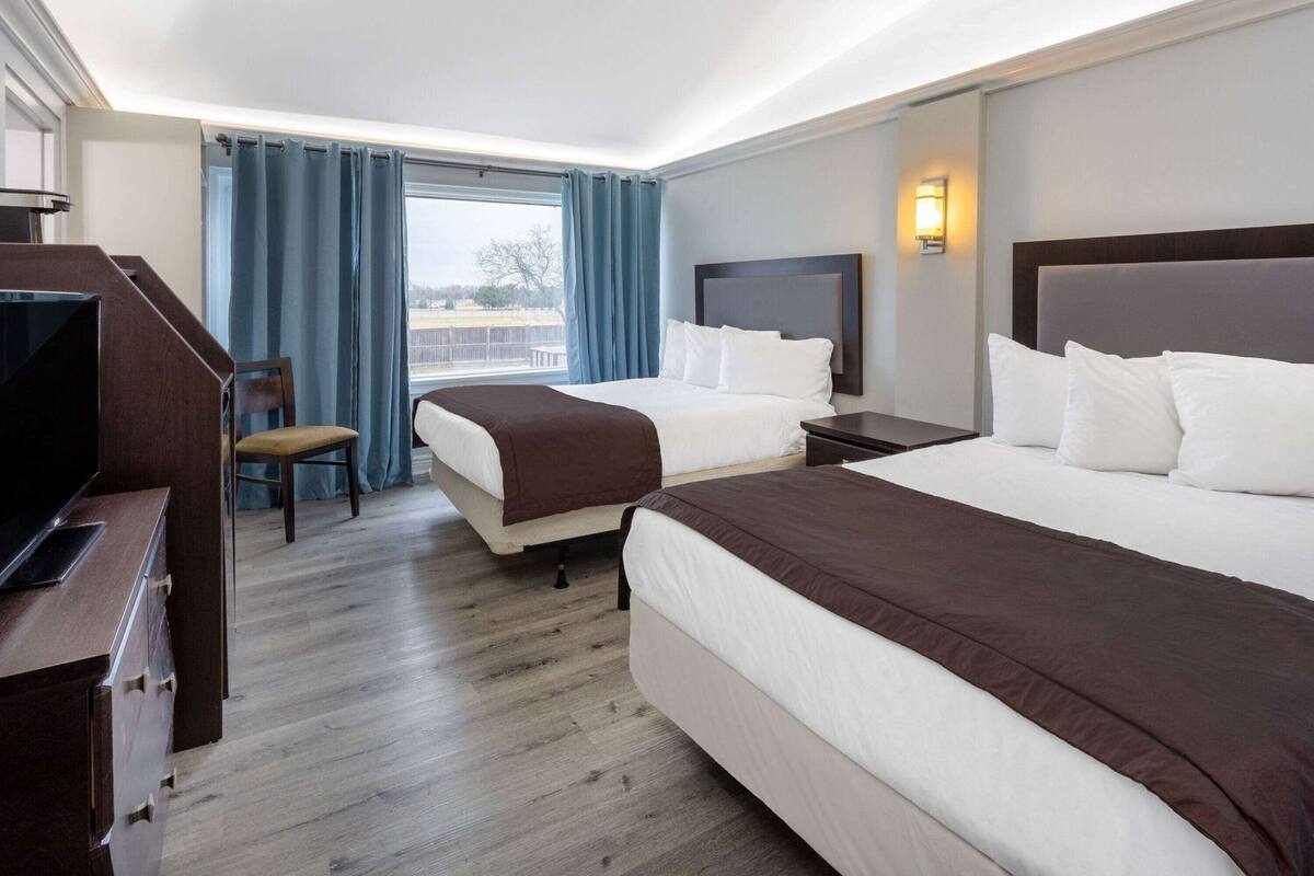 A hotel room with two beds, a TV, a desk, and a chair.