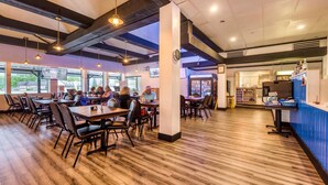 A restaurant with wooden floors, tables, and chairs. There are people dining and a counter with a menu.
