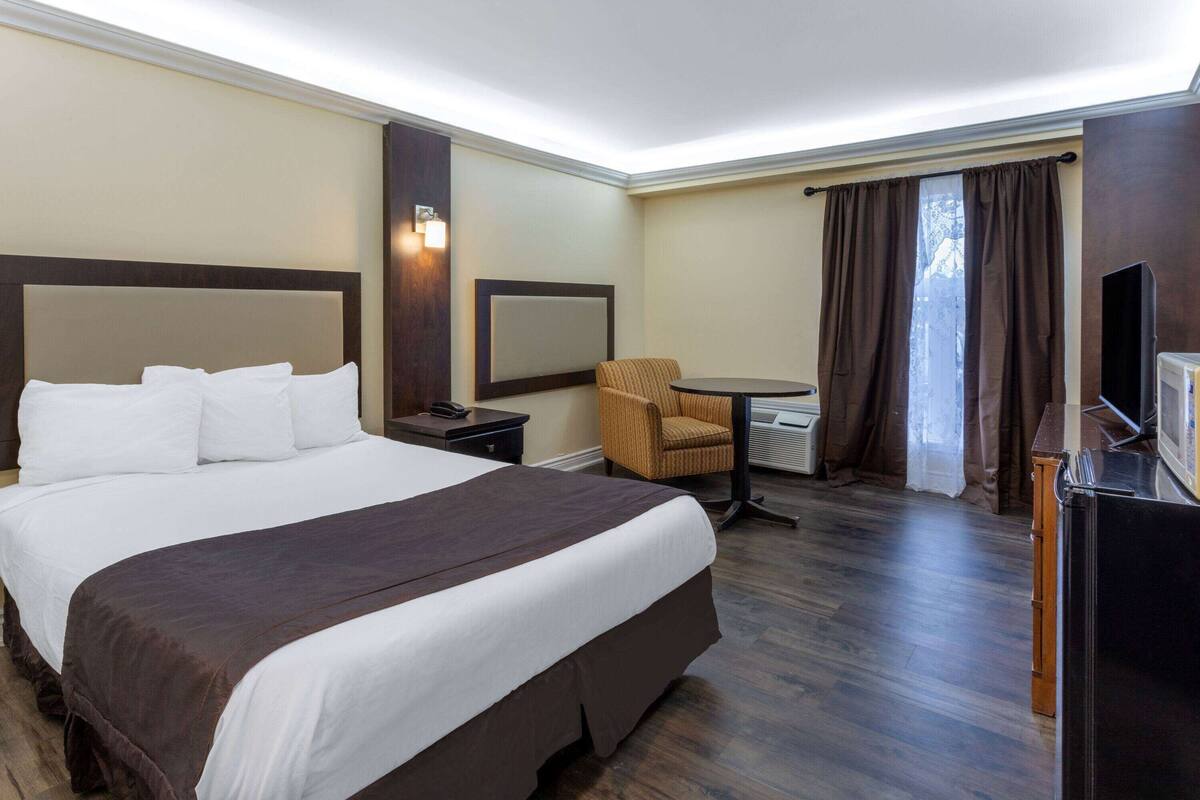 A hotel room with a large bed, a chair, a desk, a television, and a window with curtains.