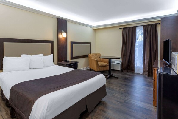 A hotel room with a large bed, a chair, a desk, a television, and a window with curtains.