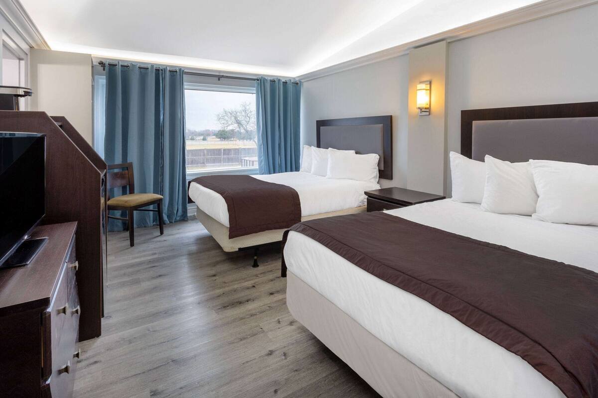 A hotel room with two beds, a desk, and a chair.