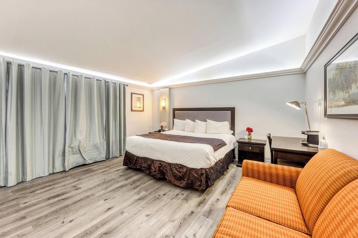A hotel room with a bed, a desk, a chair, a lamp, and a picture on the wall.