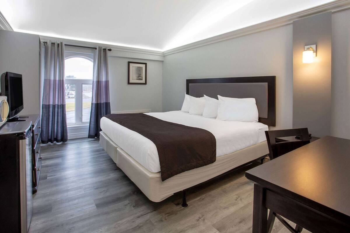 A hotel room with a bed, a desk, a chair, a television, and a window with curtains.