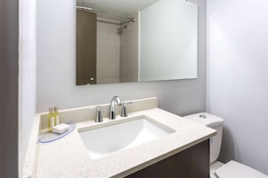A bathroom with a white sink, two faucets, a mirror, and a toilet.