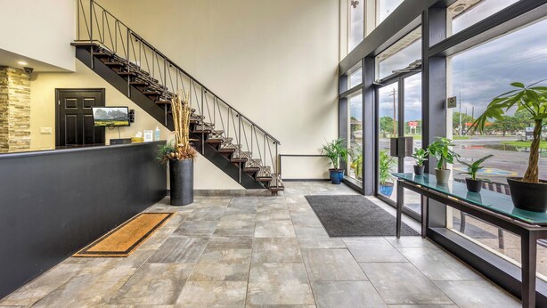 A modern lobby with a staircase, a reception desk, and large windows offering a view of the outside.