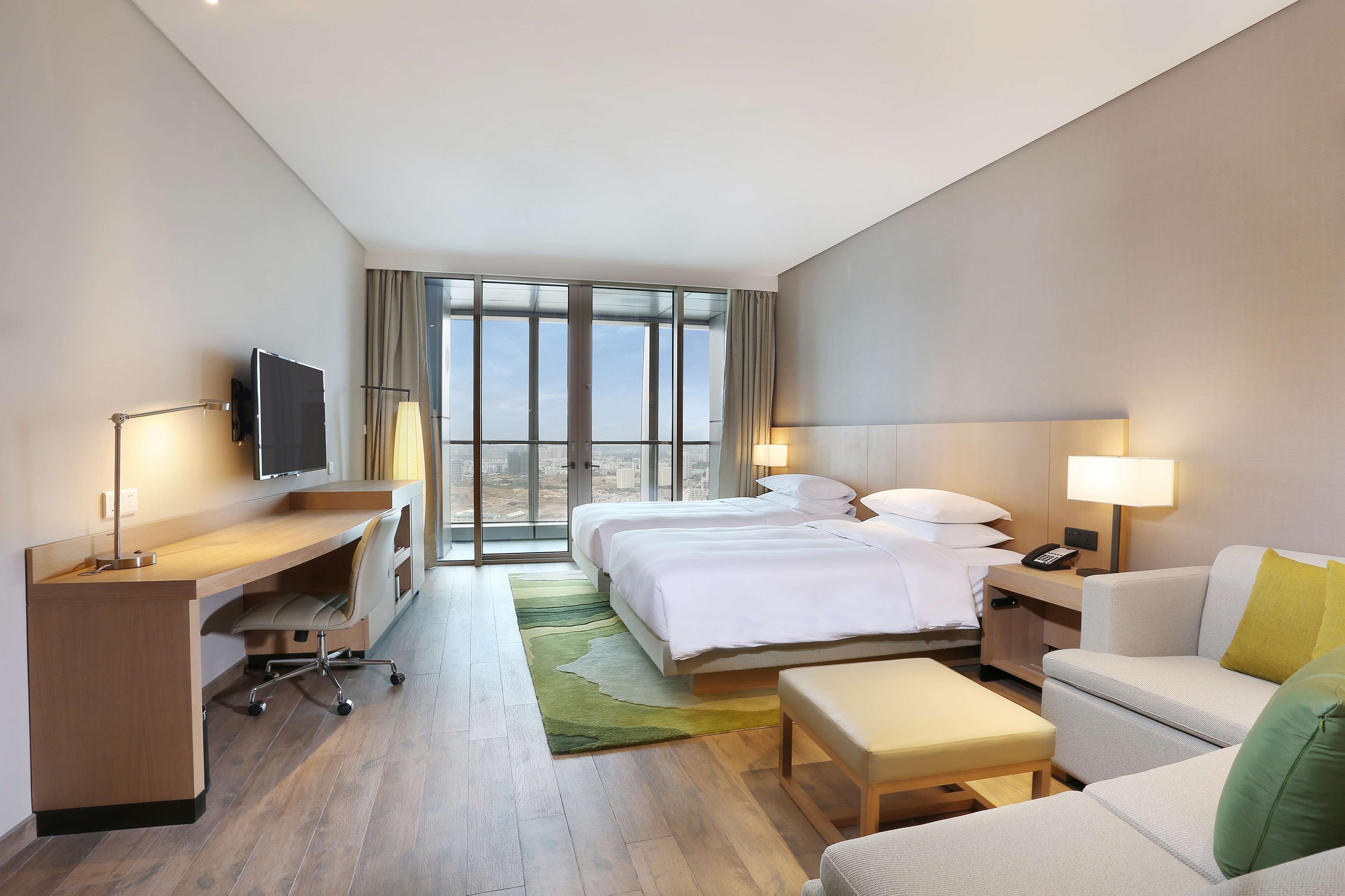 Une chambre d’hôtel équipée d’un bureau, de deux lits, d’une télévision et offrant une vue sur la ville.