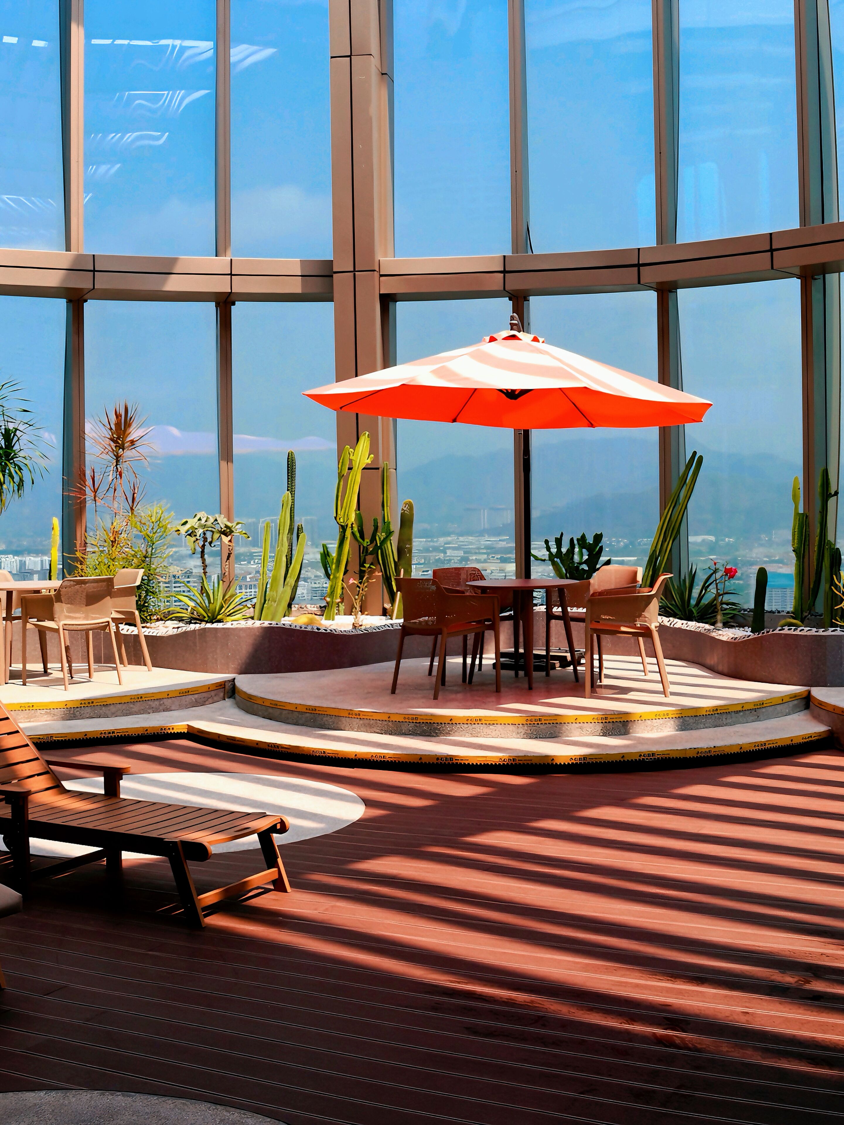 Un patio interior con mesa y sillas, rodeado de grandes ventanales y cactus.