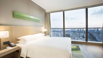 A hotel room with a large bed, a nightstand with a phone, and a view of a cityscape through a large window.