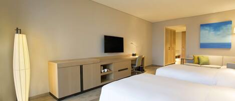 Quarto de hotel com duas camas, uma escrivaninha, uma televisão e um quadro na parede.