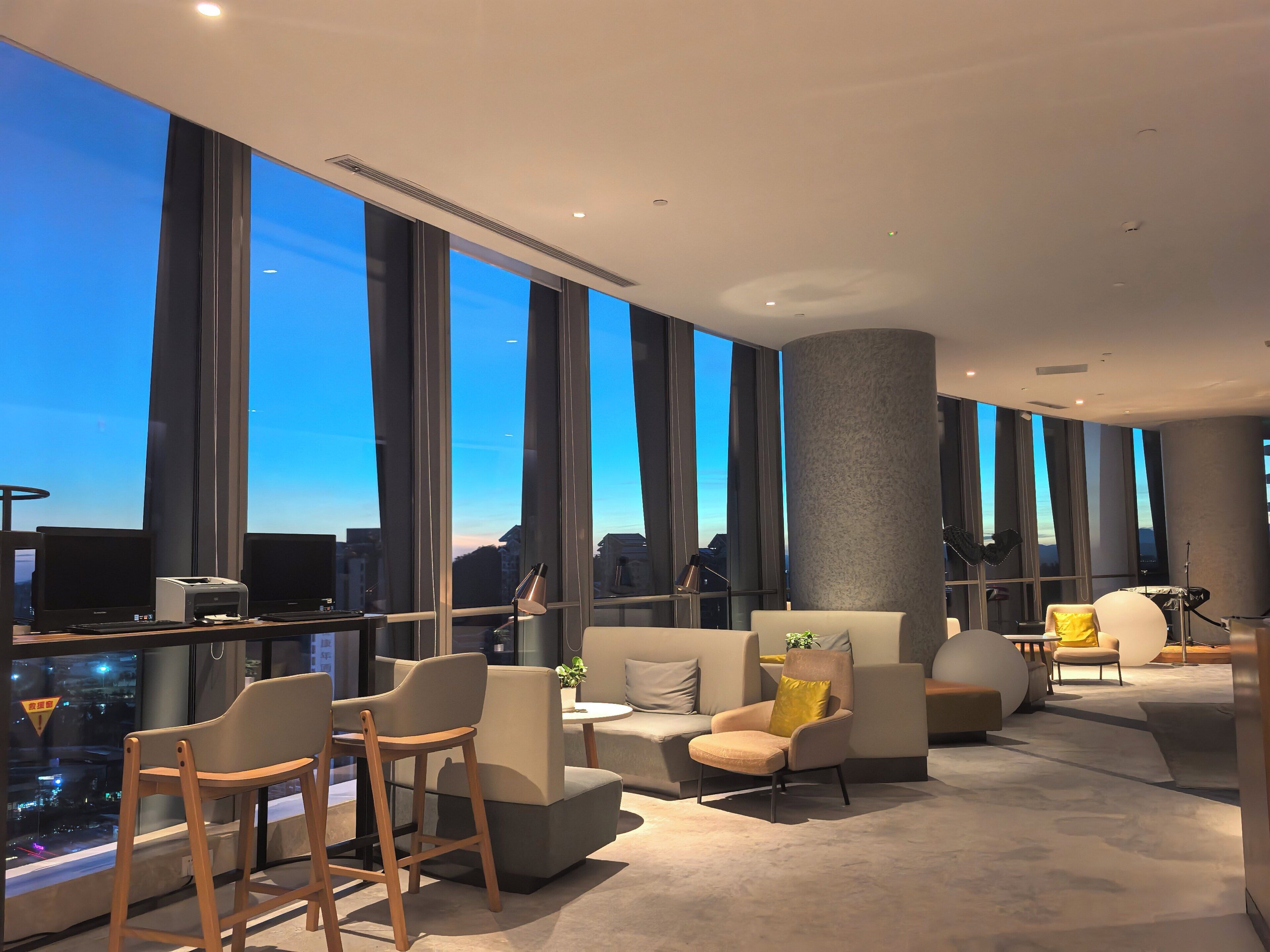 Un interior moderno con amplios ventanales, una zona de estar con sofás y sillones, y vistas a la ciudad.