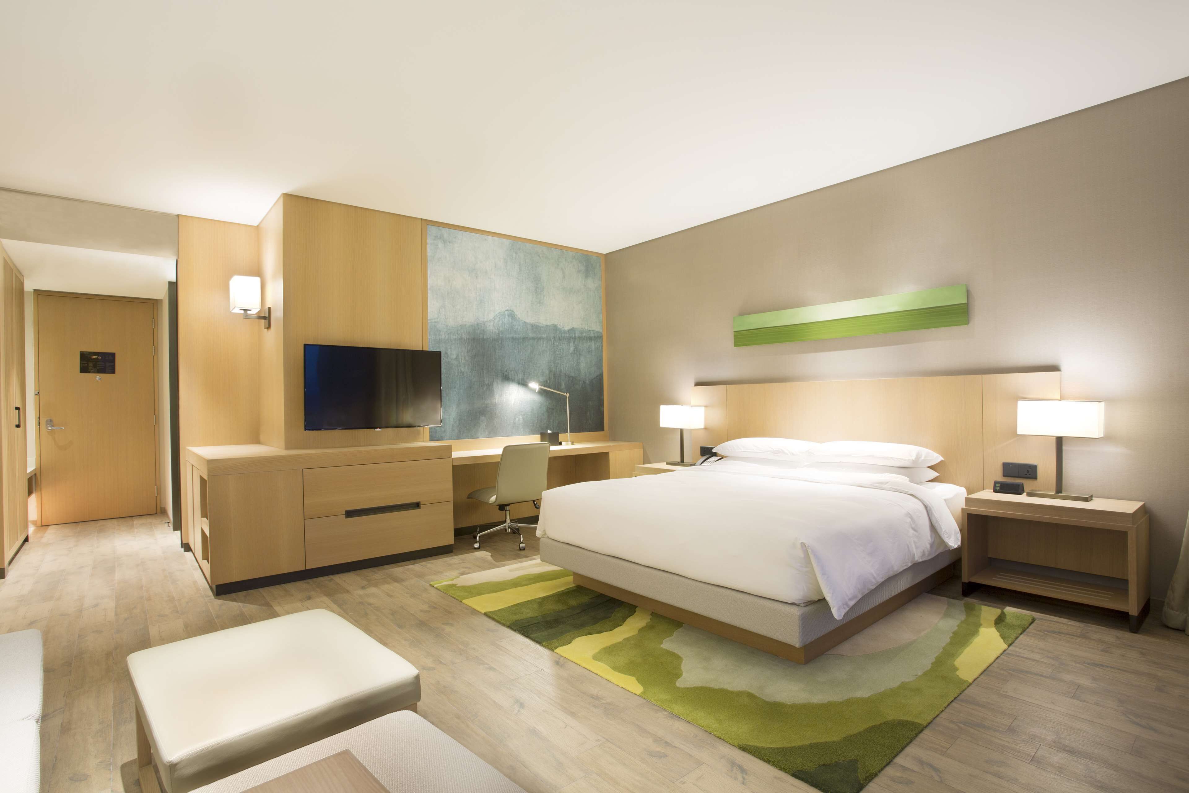 Une chambre d’hôtel moderne, dotée d’un grand lit, d’un bureau avec une chaise, d’une télévision et d’une table de chevet avec une lampe.