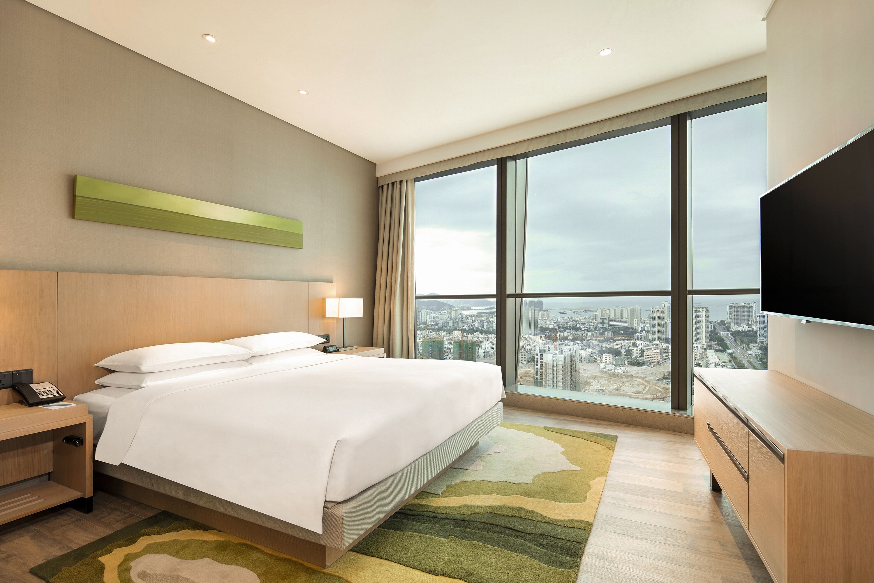 A hotel room with a large bed, a desk, a telephone, a flat-screen TV, and a city view.