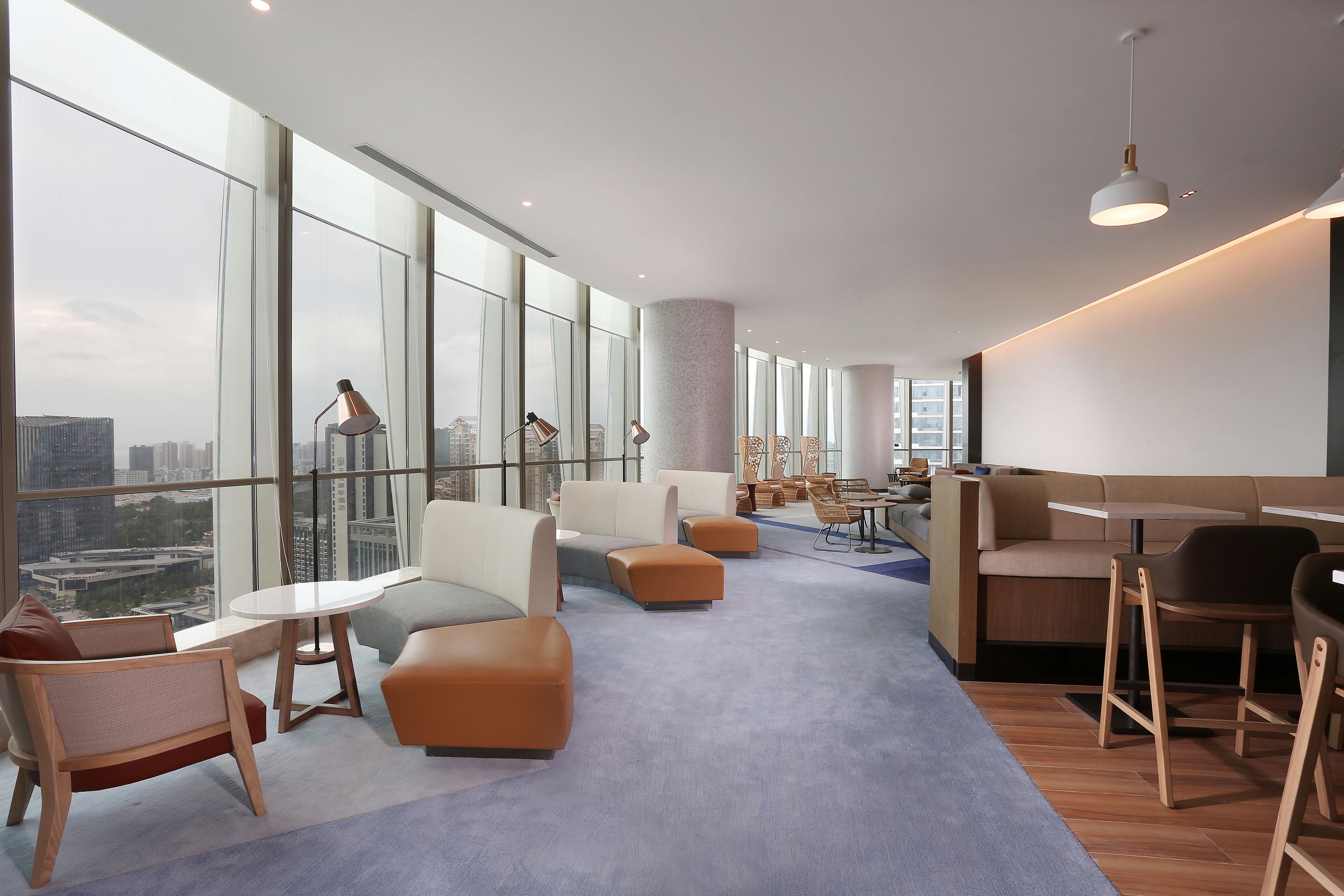 A modern lounge area with seating, tables, and large windows offering city views.