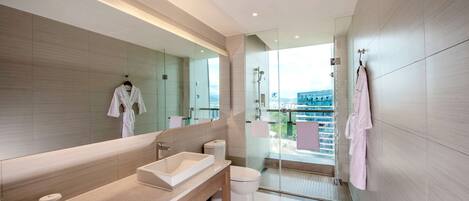 Une salle de bain moderne avec un grand miroir, un lavabo et des toilettes. Des serviettes et un peignoir sont accrochés au mur.