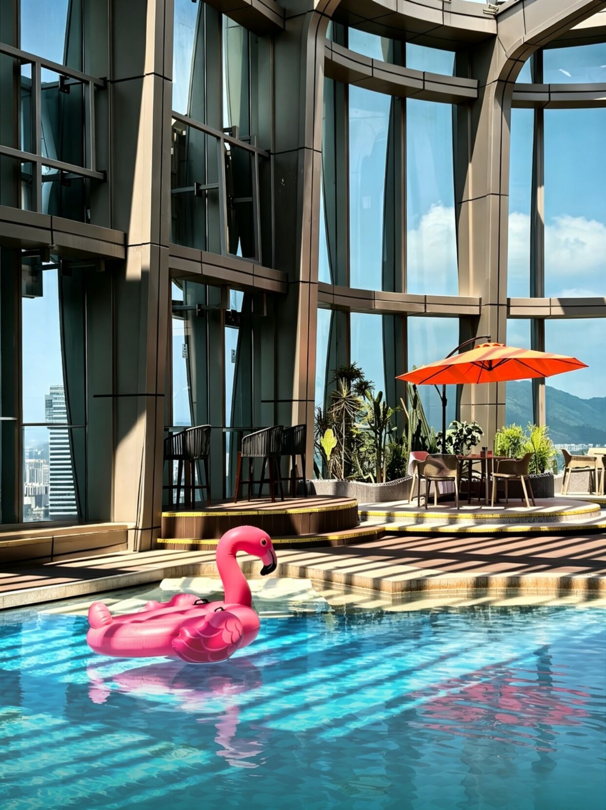 Ein modernes Gebäude mit großen Fenstern, einem Swimmingpool mit einem rosa Flamingo-Schwimmtier, Sitzgelegenheiten im Freien und Topfpflanzen.