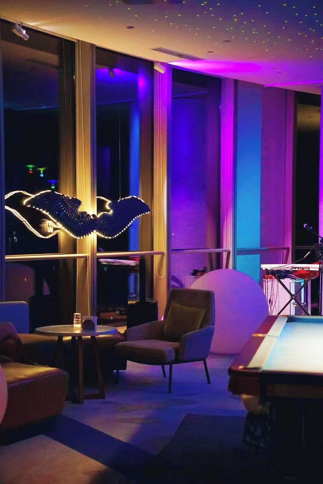 Un área de estar moderna con mesa de billar, asientos cómodos y una gran escultura iluminada.