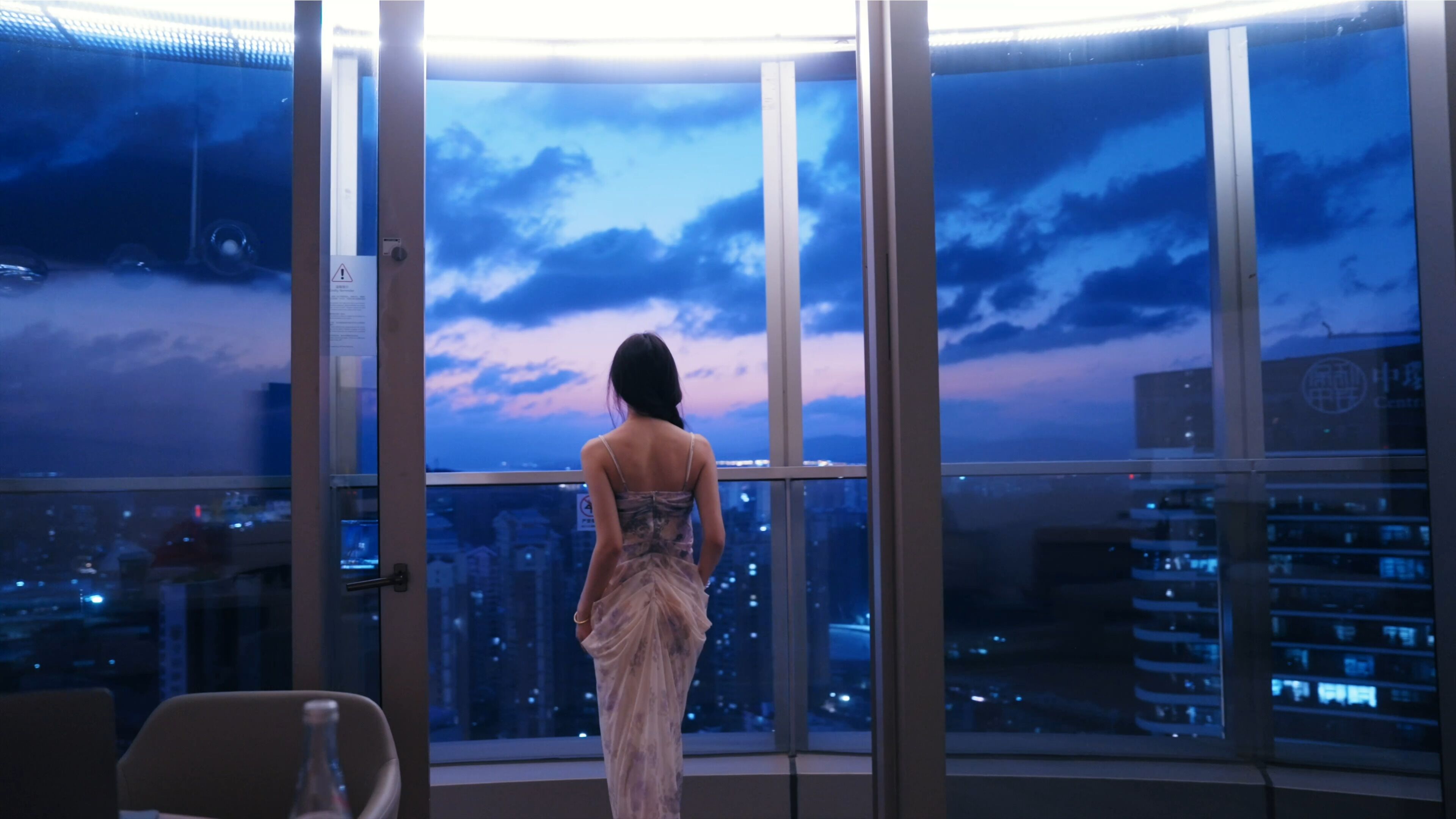 A person standing by a large window with a cityscape view.