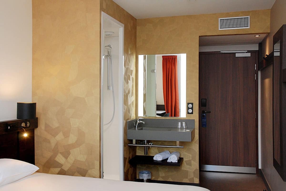 A hotel room with a bed, a shower, a sink, and a mirror.