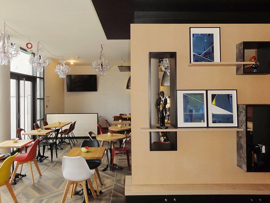 Un comedor moderno con varias mesas y sillas, un televisor de pantalla plana en la pared y lámparas de cristal decorativas.
