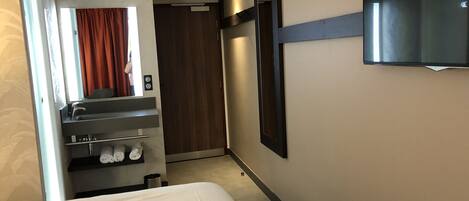 Habitación de hotel con cama, baño que incluye lavamanos y toallero, espejo, televisión y puerta que da a otra habitación.