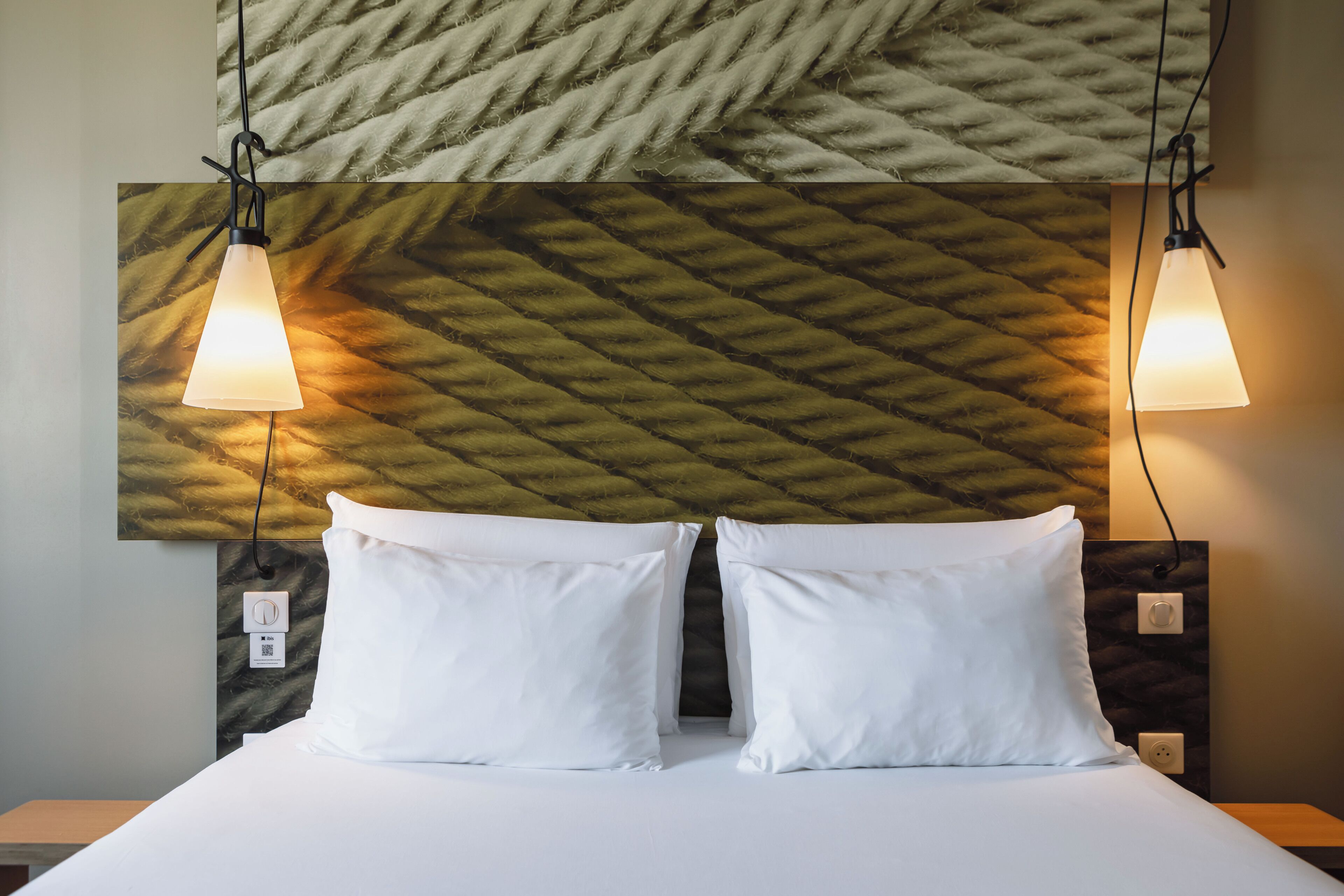 A neatly made bed with white linens, two bedside lamps, and a textured wall above.