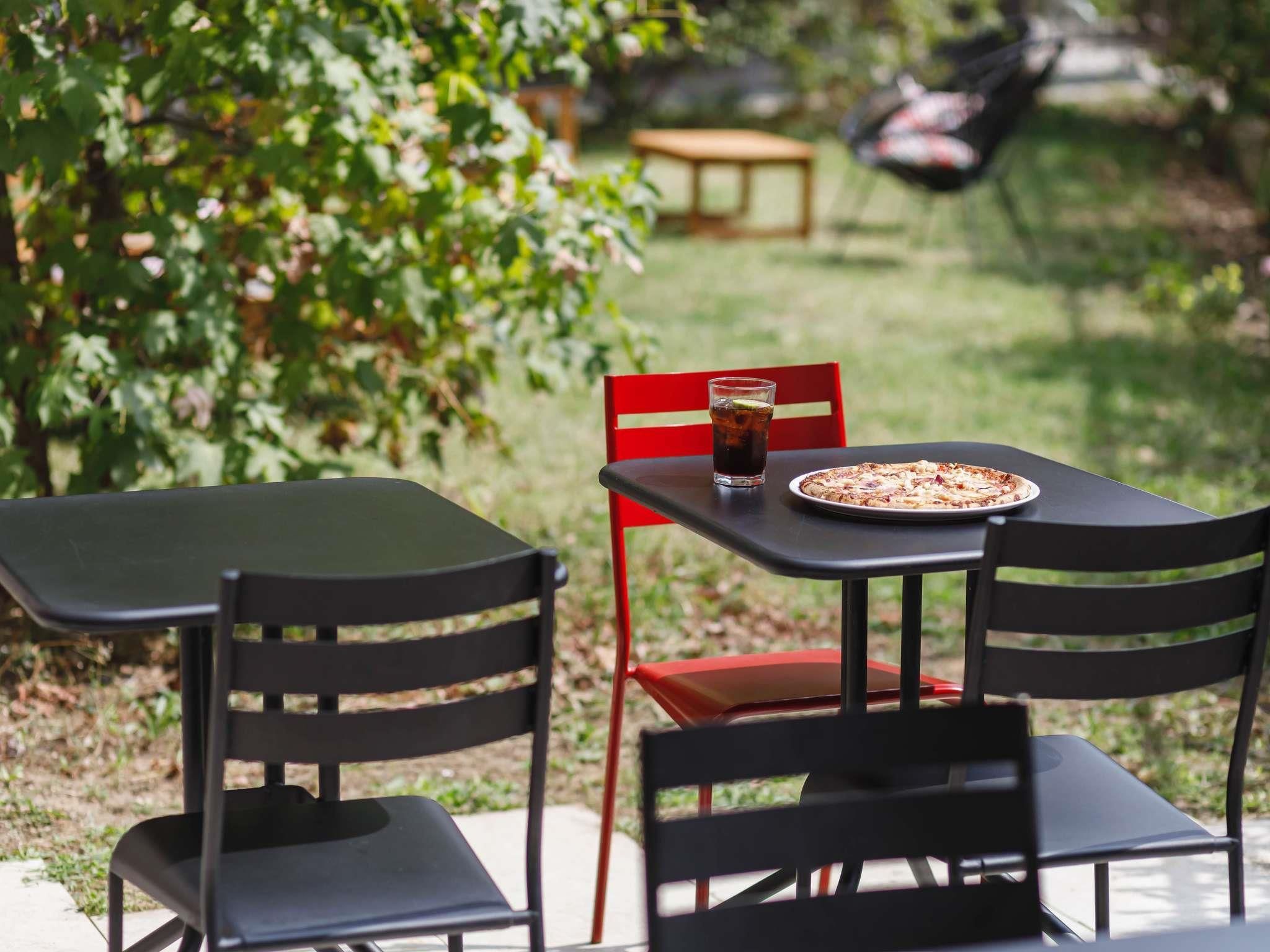 An outdoor dining area with two tables and chairs, a pizza, and a drink.