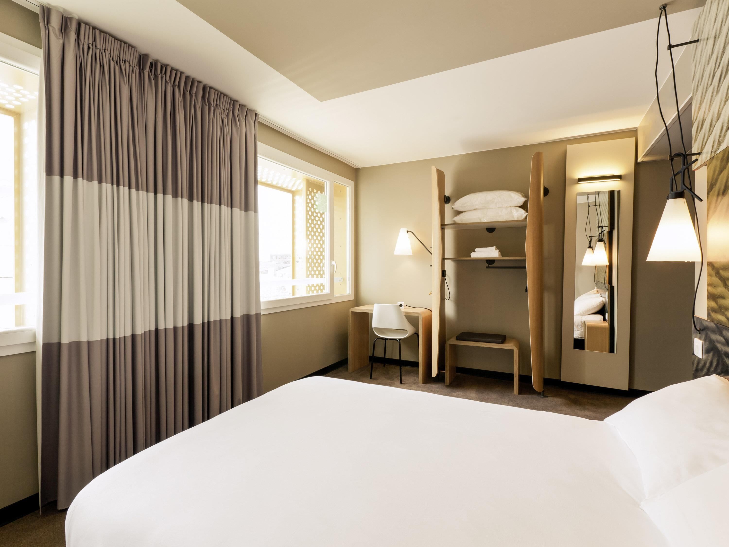 Une chambre d’hôtel avec un grand lit, un bureau, une chaise, une armoire et un miroir.