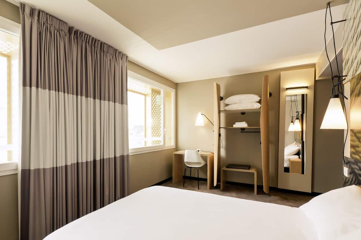 Une chambre d’hôtel avec un grand lit, un bureau, une chaise, une armoire et un miroir.