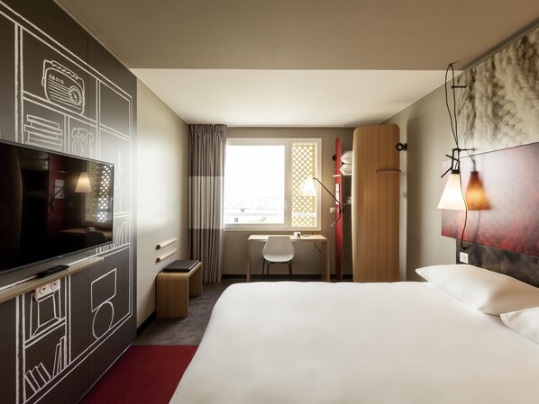 Una habitación de hotel con una cama grande, un escritorio, un televisor y una ventana con cortinas.