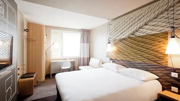 Ein modernes Hotelzimmer mit einem großen Bett, einem Schreibtisch, einem Sessel und einem kleinen Tisch.