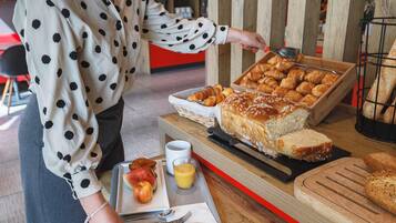 A buffet setup with various baked goods, a tray with fruits, and a beverage.