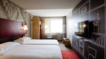 A hotel room with a large bed, a desk, a TV, and a wall with artistic drawings.