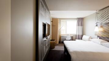 A hotel room with a large bed, a desk, a chair, a TV, and a window with curtains.