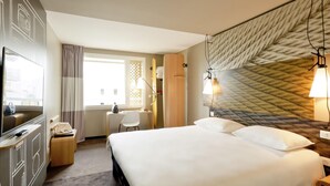 Een hotelkamer met een bed, een bureau met stoel, een televisie en een raam met gordijnen.