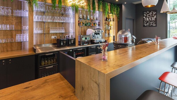 Een moderne bar met houten planken, drinkglazen en een neonbord.