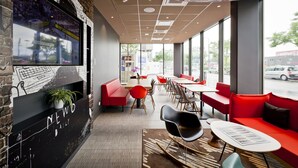Een modern café met rode zitplaatsen, een grote televisie aan de muur, en grote ramen met uitzicht op de straat.