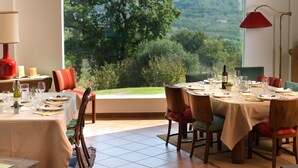 Un coin repas avec une table dressée pour quatre personnes, un lustre et une vue sur une forêt, visible à travers une grande fenêtre.
