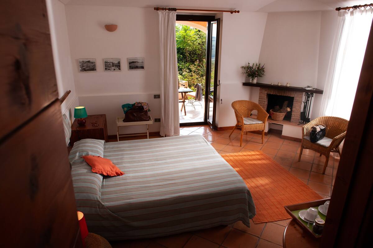 Een slaapkamer met een bed, een stoel, een tafel, een open haard en uitzicht op de omgeving.