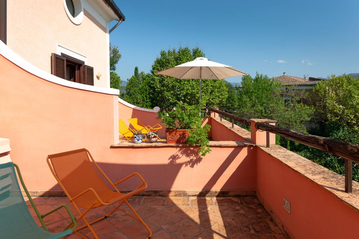 Een balkon met een stoel, een bloempot en een parasol.