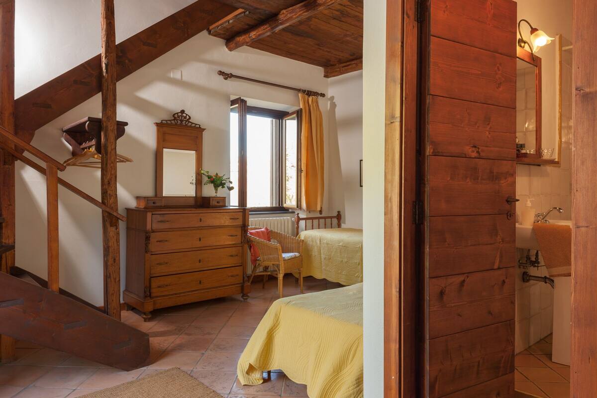 Een slaapkamer met een houten trap, een dressoir, een stoel, een bed en een raam met gordijnen.