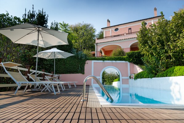 Una piscina al aire libre, sombrillas, sillones reclinables de piscina