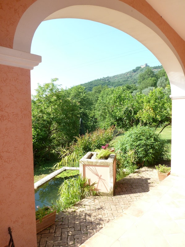 An arched view of a garden with a pond, lush greenery, and a hill in the background. - Agriturismo La Vecchia Quercia (San Cipriano Picentino)