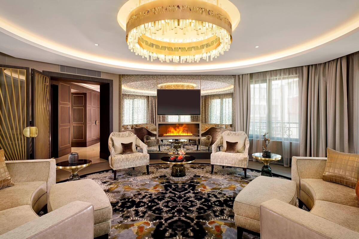 A luxurious living room with a large chandelier, a fireplace, and comfortable seating.