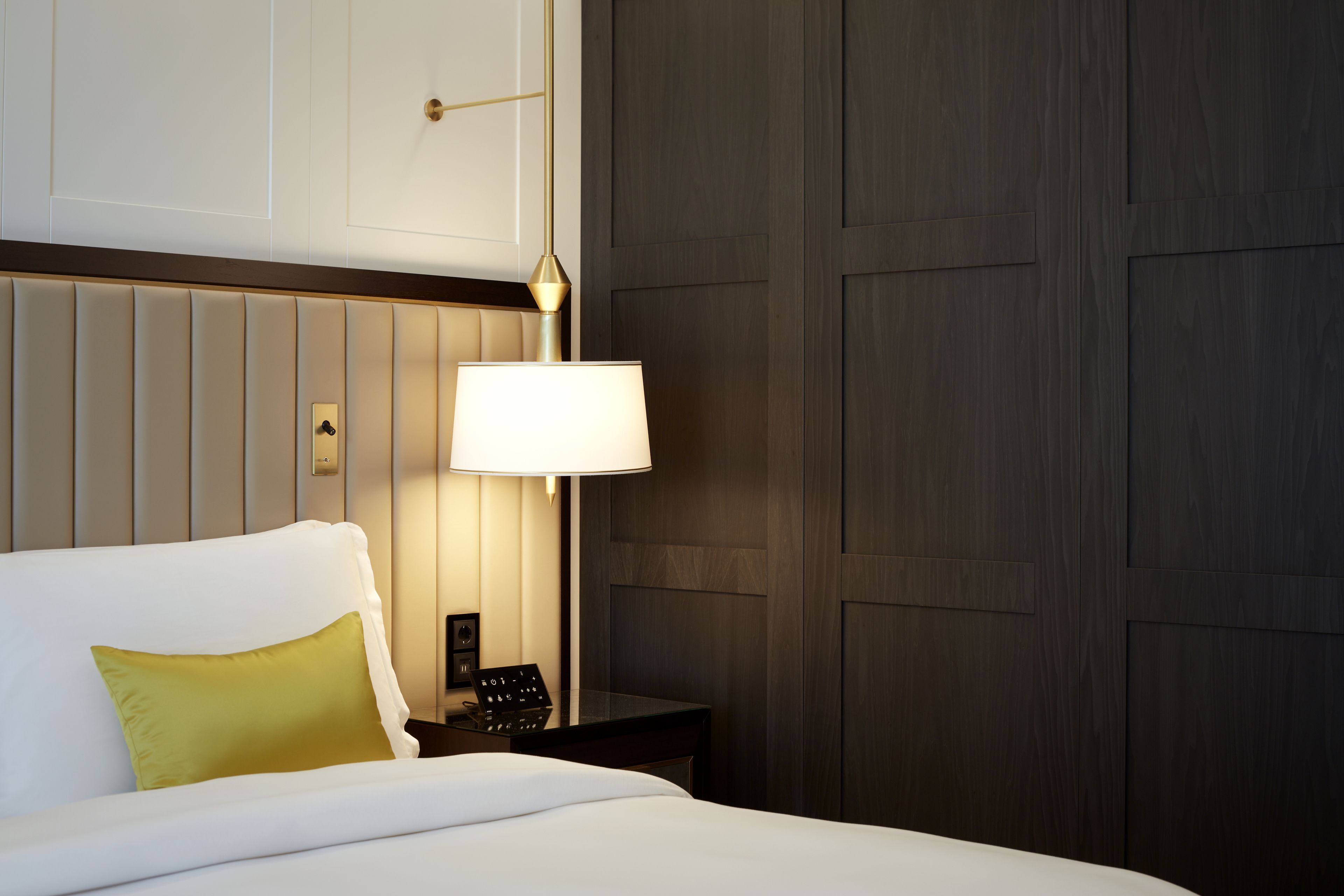 A hotel room with a bed, a bedside table with a lamp, and a wooden panel wall.