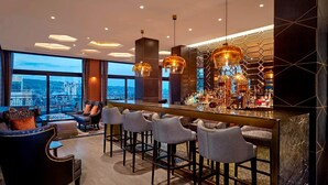A modern bar area with a city view, bar stools, and a seating area with a sofa and armchairs.