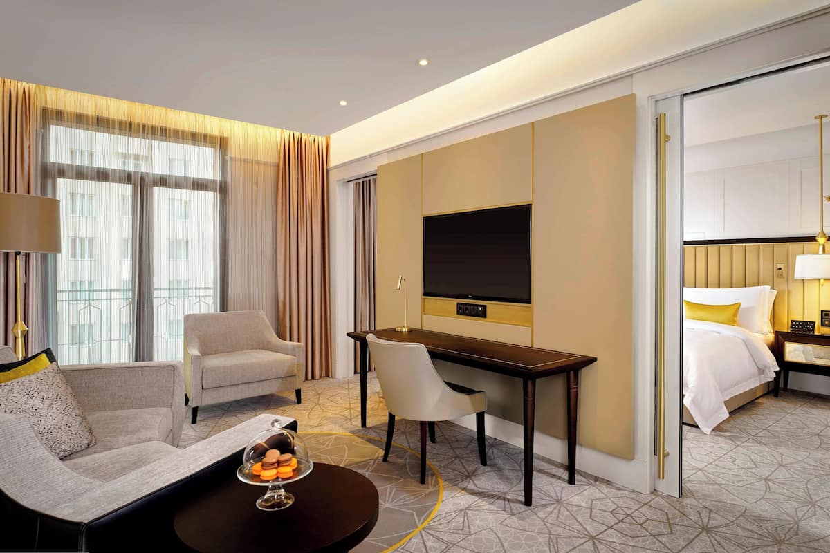 A hotel room with a sofa, a dining table with a glass dome, a desk, a TV, and a bed.