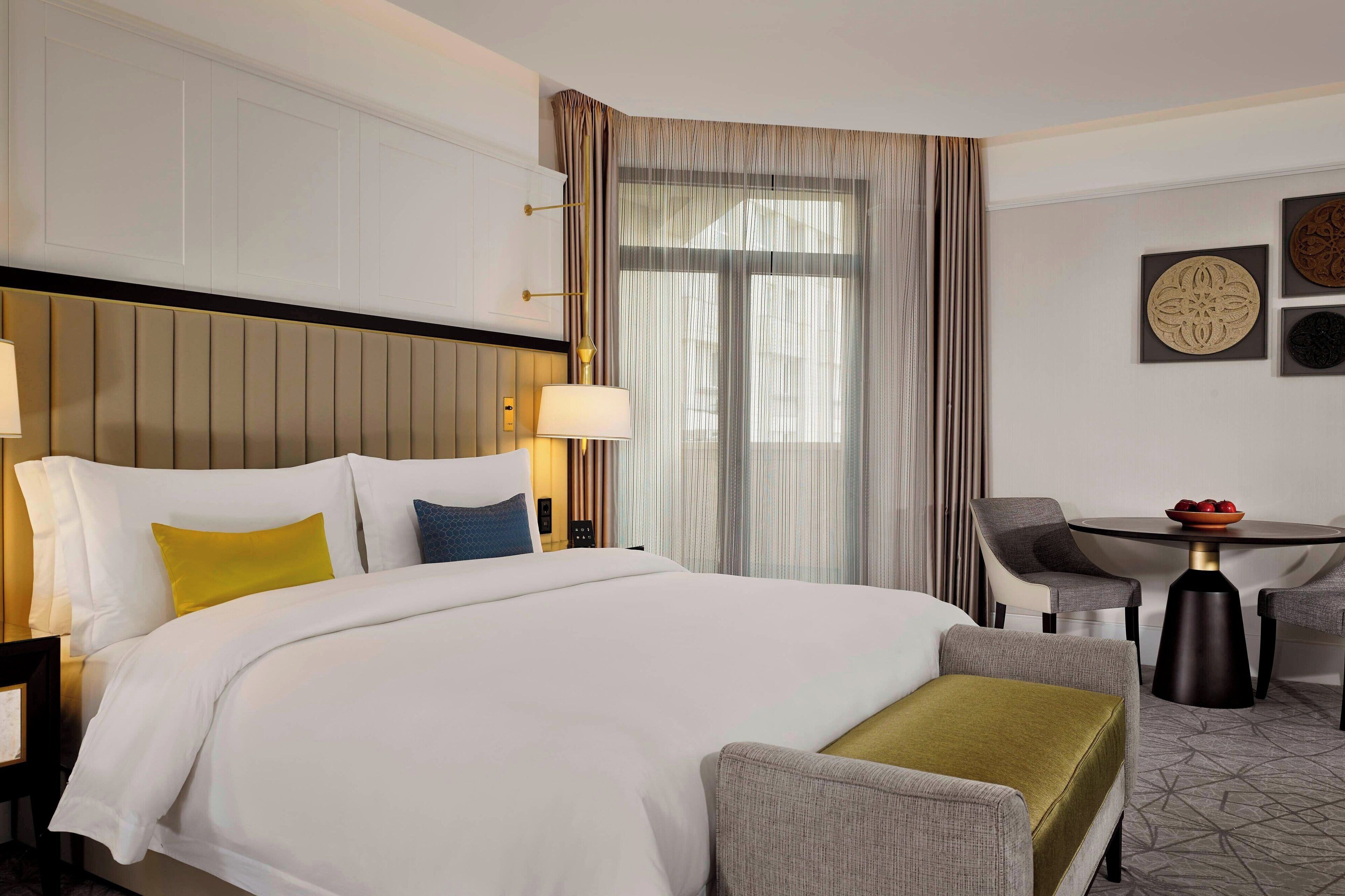 A hotel room with a large bed, a desk, two chairs, and a dining table.