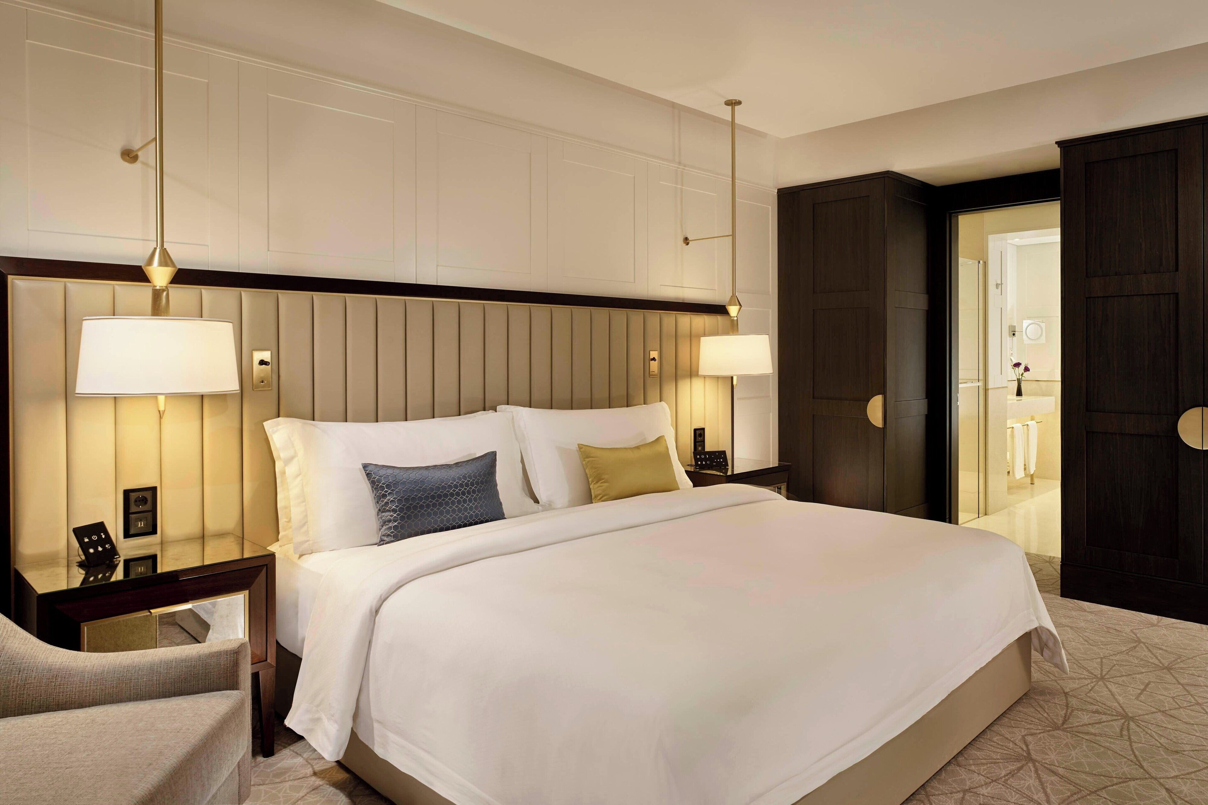 A hotel room with a large bed, two bedside tables, a nightstand, a chair, and a wardrobe.